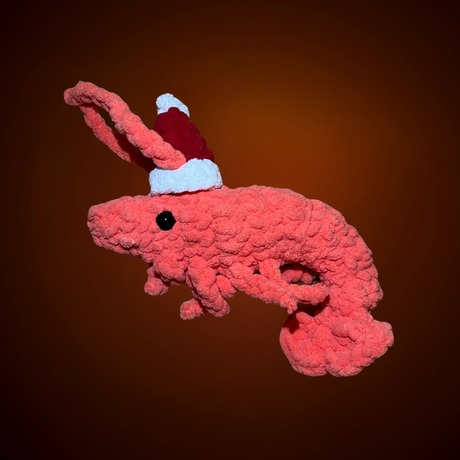 Häkelgarnele in Pink mit schwarzem Auge und rotem Weihnachtsmützchen, weiche Textur.